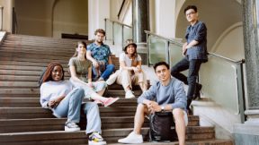 Six étudiants internationaux sont assis ensemble, détendus, sur un escalier de l'Hoschule et sourient à la caméra.