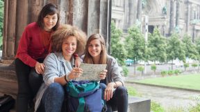 Trois étudiants internationaux sont assis avec une carte géographique dans la cour de l'ancien musée devant la cathédrale de Berlin.