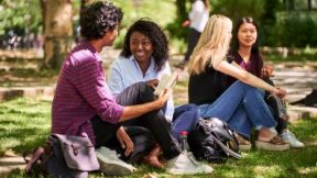 Des étudiants internationaux sont assis ensemble sur une pelouse du campus.
